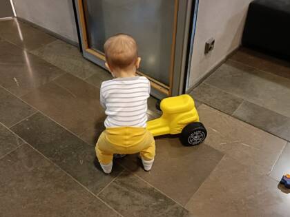 Ett litet barn skuffar på en gul plastmoped.