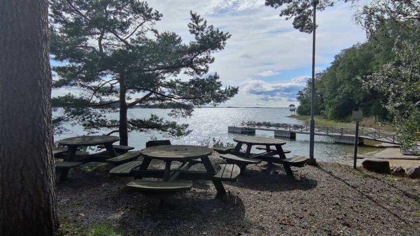 Meren rannalla puisia pöytiä ja tuoleja. Taustalla laituri.