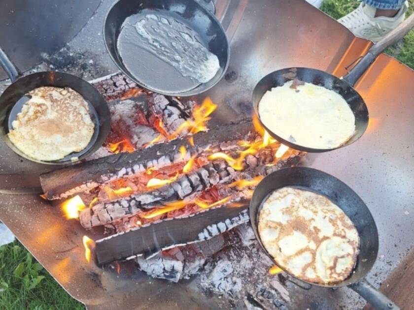 Räiskäleitä paistetaan pannuissa avotulen päällä
