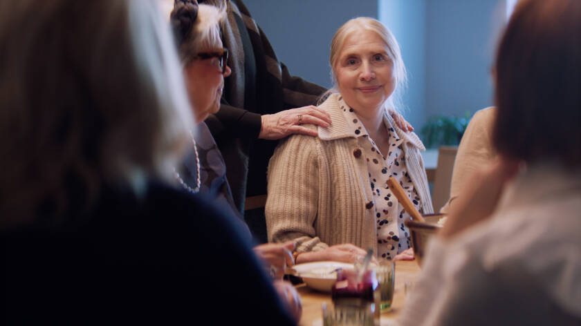 En äldre dam sittande vid ett kaffebord.