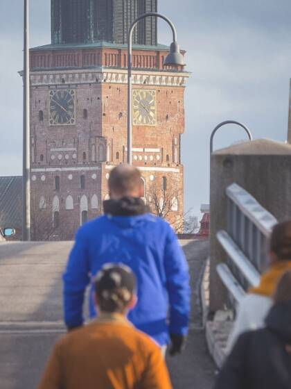 Ihmisiä kävelee sillan yli. Taustalla häämöttää Turun tuomiokirkon torni valtavana.