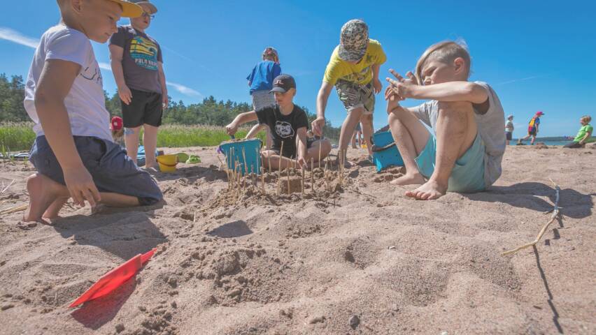 Ryhmä kouluikäisiä poikia rakentaa hiekkalinnaa rannalla.