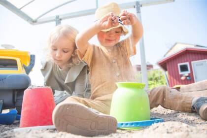 Kaksi lasta istuu hiekkalaatikossa leikkimässä. Toisella lapsista on kehitysvamma.