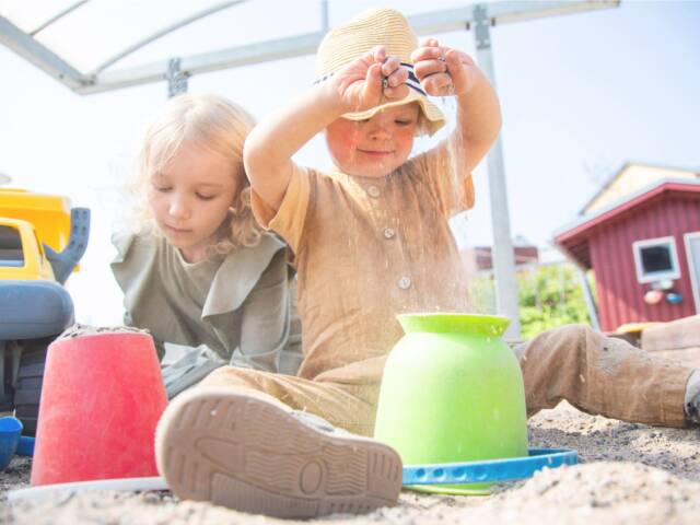 Kaksi lasta istuu hiekkalaatikossa leikkimässä. Toisella lapsista on kehitysvamma.