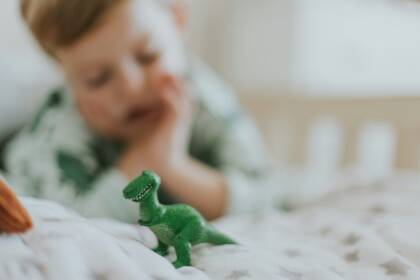 Sängyllä makoileva lapsi katsoo leludinosaurusta.