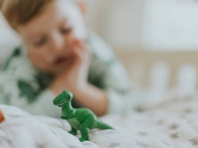 Sängyllä makoileva lapsi katsoo leludinosaurusta.
