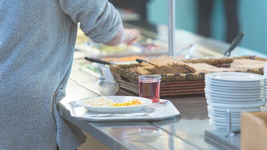 Henkilö täyttää lautasensa buffet-pöydässä, jossa on erilaisia ruokia ja juomia. Taustalla näkyy muita asiakkaita.