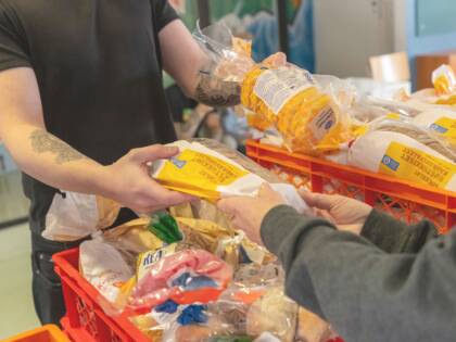 Henkilö ojentaa toiselle henkilölle kahta leipäpussia. Ympärillä on koreissa leipäpusseja.