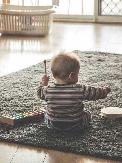 En baby som sitter på en matta och trummar.