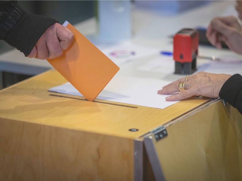 Käsi laittaa äänestyslipukkeita vaaliuurnaan.