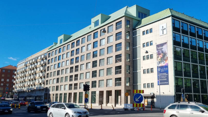 Vaalea, tiiliverhoiltu kerrostalo. Edustalla autotie.