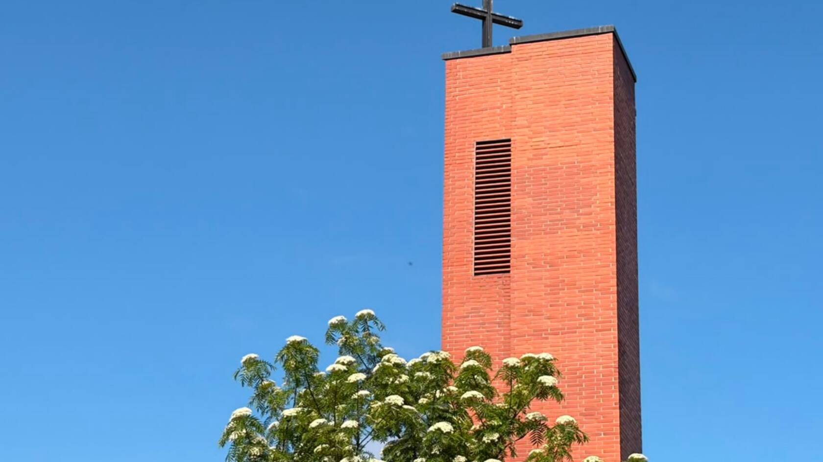 henrikinkirkon tapuli sinistä taivasta vasten, pihlaja kuukkii etualalla.