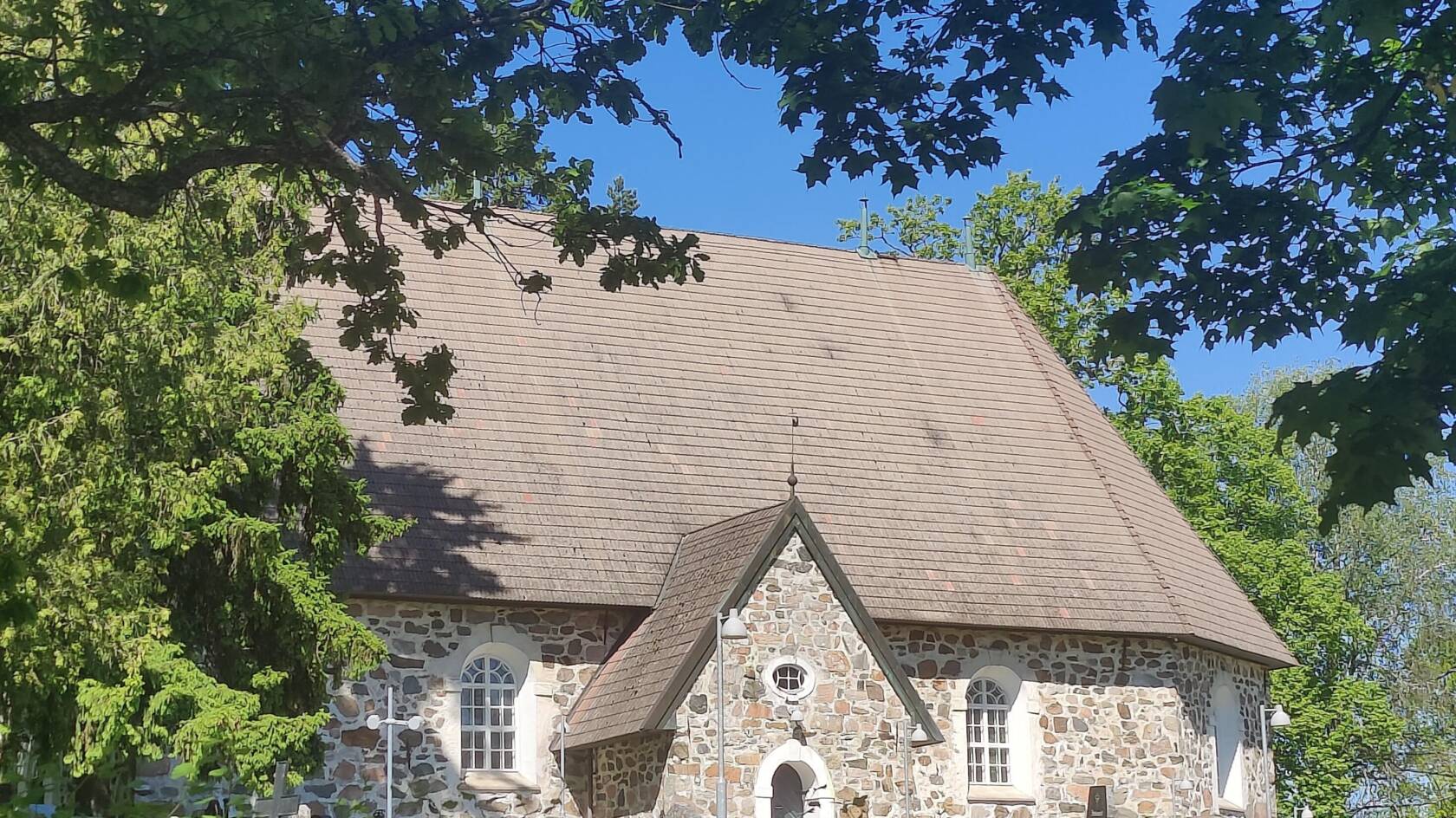 kivikirkko vehreiden puiden keskellä, kirkas taivas.