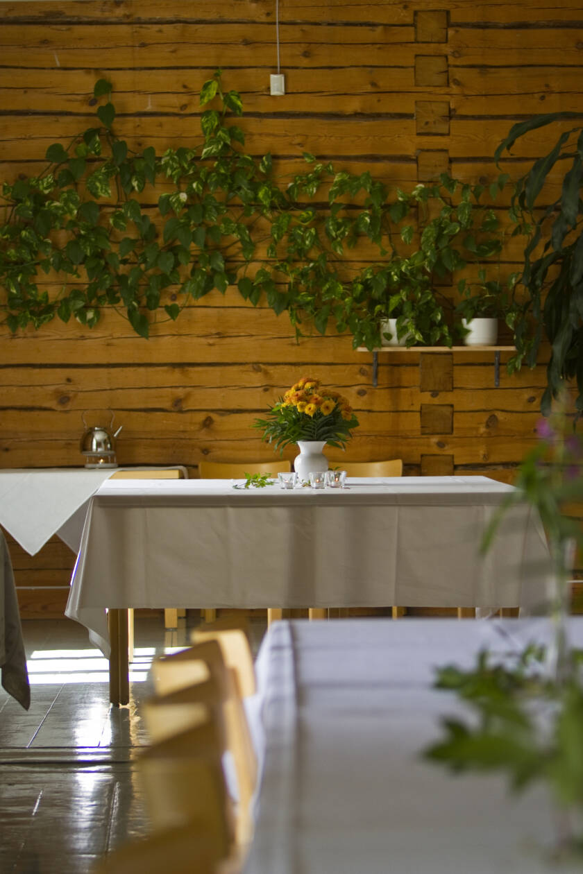 En vacker lokal med träpanelväggar, ett vitt duk och en blomsterbukett på bordet. Gröna växter i bakgrunden.