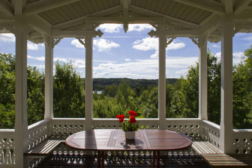 Vacker utsikt från terrassen med ett träbord och en blomkruka. I bakgrunden syns en grönskande landskap och en klar himmel.