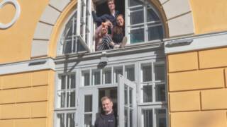 Maaherran Makasiinin keltainen vanha rakennus. Ikkunassa ja ovella nuoria aikuisia hymyillen.