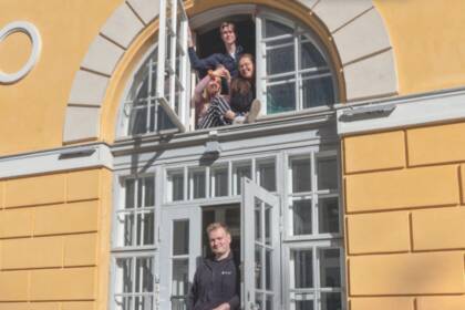 Maaherran Makasiinin keltainen vanha rakennus. Ikkunassa ja ovella nuoria aikuisia hymyillen.