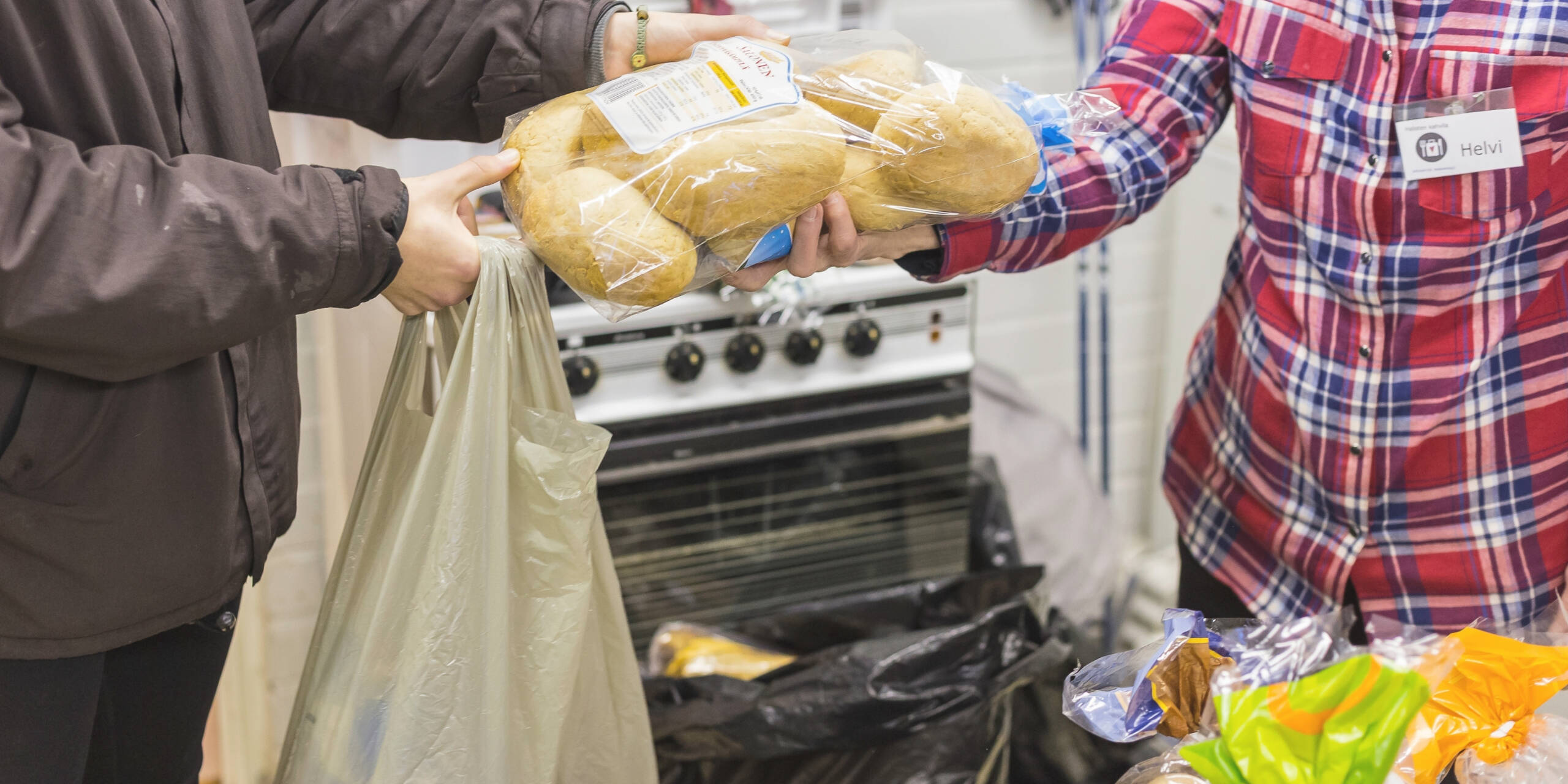 Ruokakassijakelua. Vapaaehtoinen ojentaa asiakkaalle leipapakkausta.