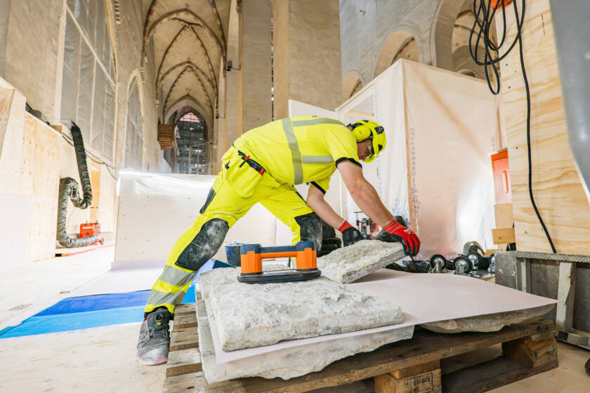 A man wearing yellow workwear lifts a limestone slab.