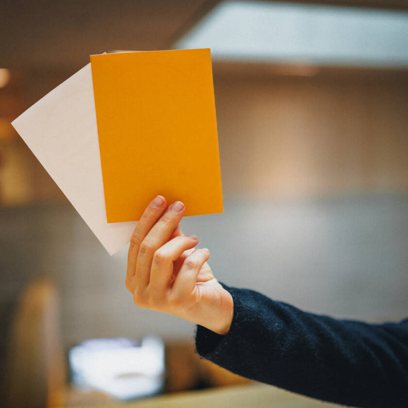 Handen håller två valblanketter: den vita och den orange